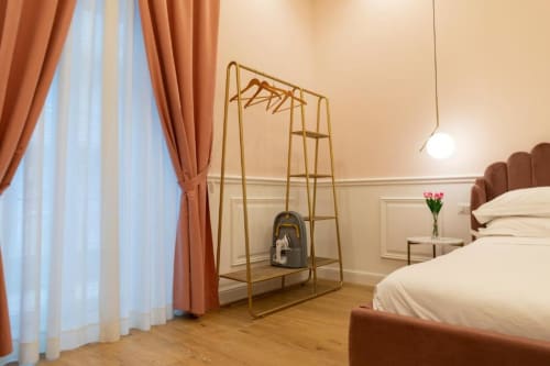 Camera moderna della Mas Collection a Bari con letto bianco, tende in terracotta, appendiabiti dorati e pavimento in legno
