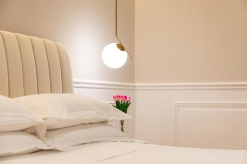 Camera da letto moderna beige della Mas Collection Bari con biancheria color crema, testata rigata, lampada a sospensione e fiori rosa
