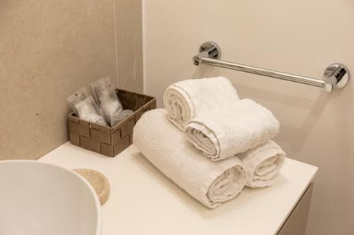 Asciugamani bianchi arrotolati esposti sul bancone del bagno nella camera beige di Mas Collection a Bari, con cestino di amenities