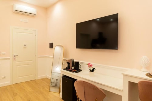 Camera da letto moderna con TV a parete, scrivania con sedia, specchio e parete accent rosa alla Mas Collection di Bari