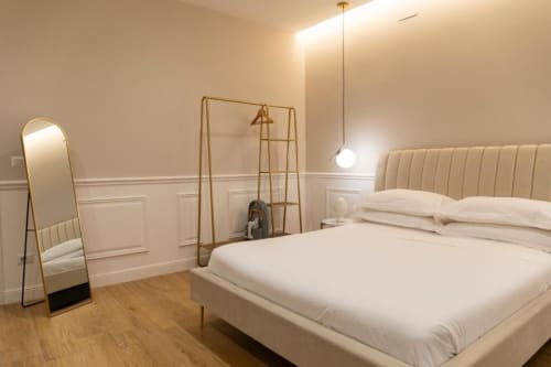 Camera moderna beige di Mas Collection Bari con letto color crema, specchio dorato, lampada a sospensione e pavimentazione a spina di pesce