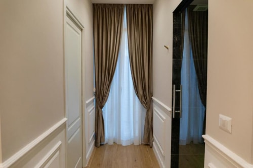 Corridoio dell'appartamento Mas Collection Bari con pareti beige, tende tortora e vista sulla corte interna attraverso le finestre