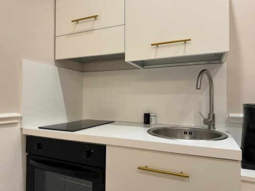 Kitchenette moderna in tonalità beige con lavello in acciaio inox, forno nero e maniglie in ottone nell'apartamento Mas Collection, Bari