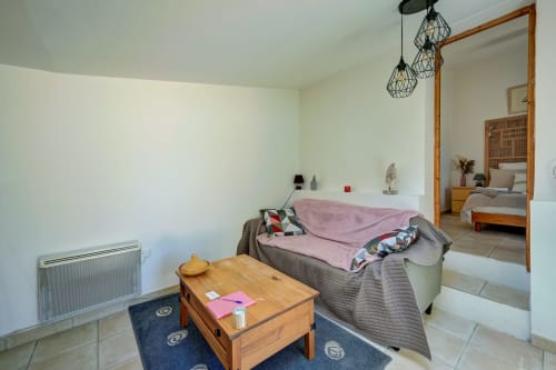 Séjour du cottage avec canapé gris, table basse en bois, luminaires géométriques et vue sur la chambre au Domaine Bellavigne