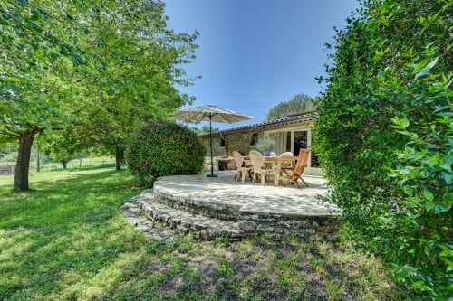 Terrasse toscane du Domaine Bellavigne avec coin repas, parasol, patio en pierre et haies taillées à Forcalquier
