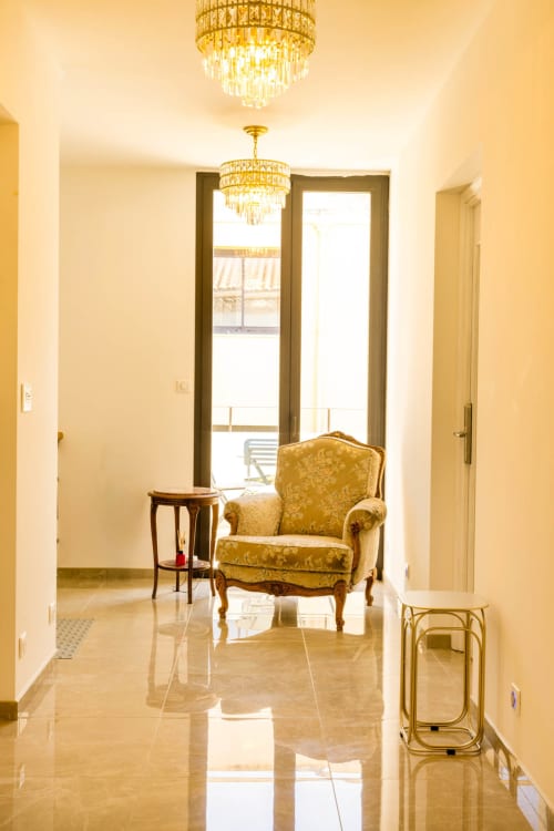 Elegante corridoio dell'Hôtel Villa Martini ad Ajaccio con lampadari in cristallo, poltrona dorata e pavimento in marmo