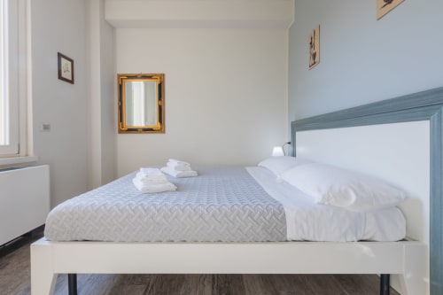 Camera luminosa all'hotel Prince Garda a Solarolo con letto bianco, testata blu e specchio dorato su pareti color crema
