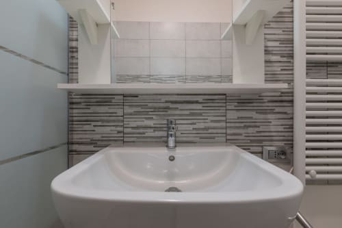 Vanity moderna del bagno con lavabo bianco curvo, rivestimento in piastrelle a righe e specchio all'hotel Prince Garda, Solarolo