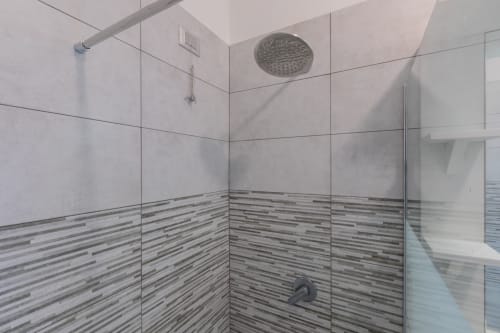 Moderno box doccia in vetro presso l'Hotel Prince Garda a Solarolo con parete piastrellata a strisce e soffione pioggia.