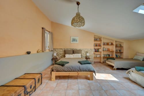 Chambre spacieuse aux Gîtes Domaine Bellavigne avec lit en bois, tête de lit en pierre, bibliothèques et décor rustique à Forcalquier