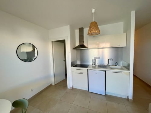 Cucina moderna nell'appartamento di Marina di Bravone con armadi bianchi, elettrodomestici in acciaio inox e lampada a sospensione intrecciata.