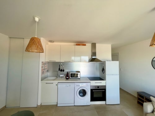 Cuisine moderne avec armoires blanches, lave-linge et luminaire suspendu tressé à l'appartement Résidence Marina di Bravone