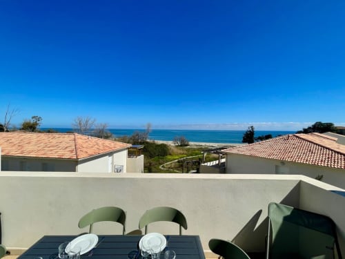 Vue panoramique sur la mer depuis la terrasse de la Résidence Marina di Bravone avec table à manger et paysage côtier