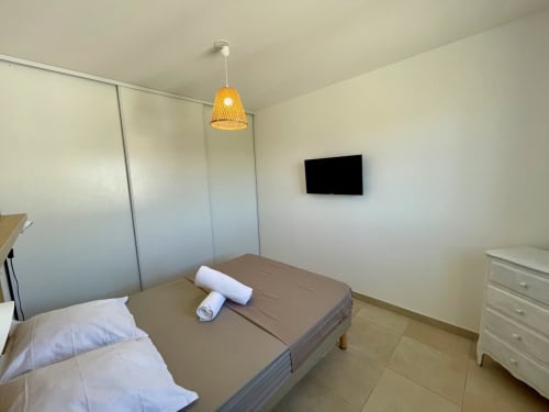 Camera moderna alla Résidence Marina di Bravone con letto, lampada a sospensione intrecciata, TV a parete e cassettone bianco