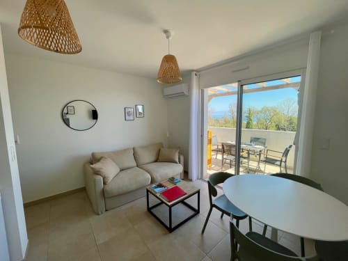 Moderno soggiorno a Marina di Bravone, Linguizzetta con divano beige, specchio rotondo, lampade a sospensione intrecciate, zona pranzo