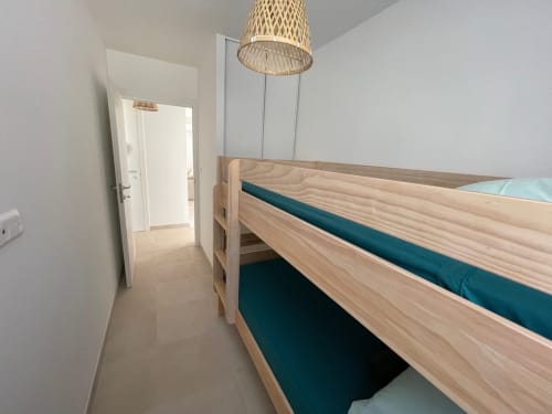 Modern bedroom at Résidence Marina di Bravone with light wood bed, teal bedding, woven pendant light, and neutral décor