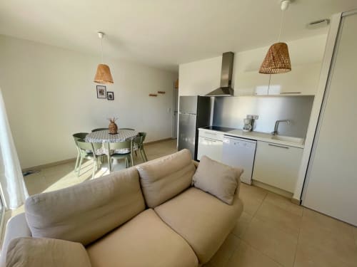Modern open-plan apartment at Résidence Marina di Bravone with beige sofa, dining area, kitchen, pendant lights, and