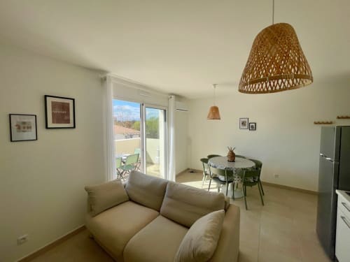 Bright open-plan apartment at Résidence Marina di Bravone with cream sofa, dining area, woven pendant lights, and sea view