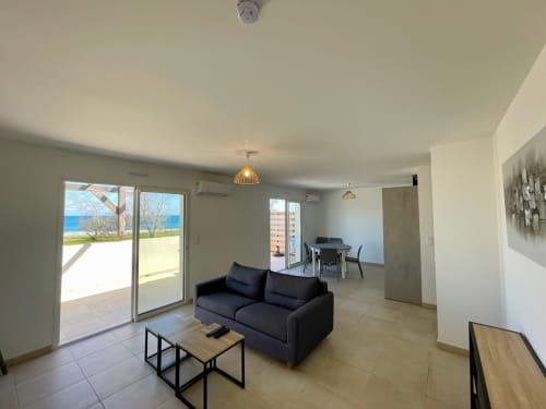 Appartamento con vista mare moderno a Résidence Marina di Bravone con divano nero, zona pranzo e terrazza con vista sulla Corsica