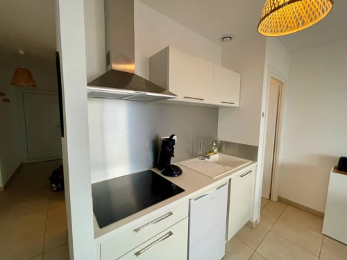 Kitchenette moderne de l'appartement T3 Marina di Bravone avec électroménagers blancs, plan de travail noir et luminaires suspendus
