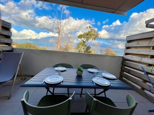 Terrasse extérieure à Marina di Bravone avec table dressée, vue sur la mer et montagnes en arrière-plan