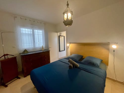 Camera accogliente presso la Résidence Marina di Bravone a Linguizzetta con biancheria blu, testata in legno e lampada a sospensione in ottone