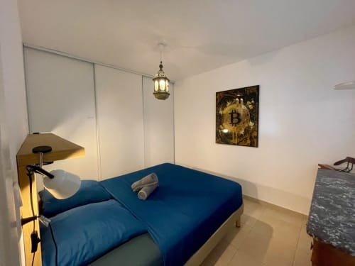 Camera accogliente in Résidence Marina di Bravone con letto blu, lampada a sospensione e opera d'arte Bitcoin