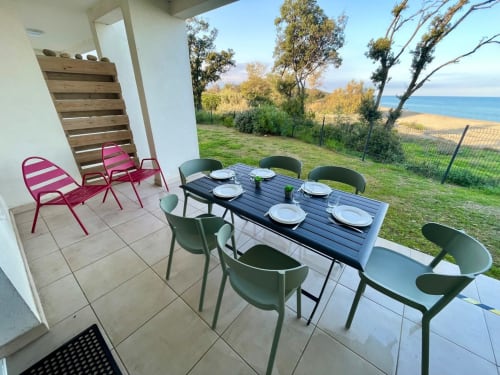 Beachfront apartment terrace at Marina di Bravone with dining table, green chairs, and sea views in Linguizzetta, Corsica