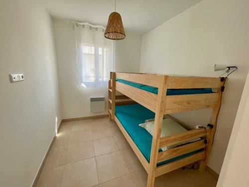 Bright bedroom in beachfront apartment at Résidence Marina di Bravone with wooden bunk bed, turquoise bedding, and tile