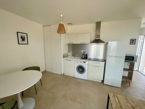 Kitchenette moderne avec armoires blanches, électroménagers en acier inoxydable et coin repas à Résidence Marina di Bravone,