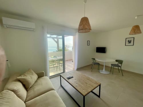 Appartement Marina di Bravone avec vue mer, salon moderne avec canapé blanc, coin repas et balcon panoramique