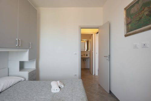 Camera da letto moderna nell'appartamento Maestrale a Finale Ligure, con letto, mobili bianchi e porta aperta verso il bagno ensuite