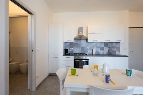 Cucina open-plan moderna e zona pranzo dell'appartamento Maestrale a Finale Ligure, con mobili bianchi e vista sul mare