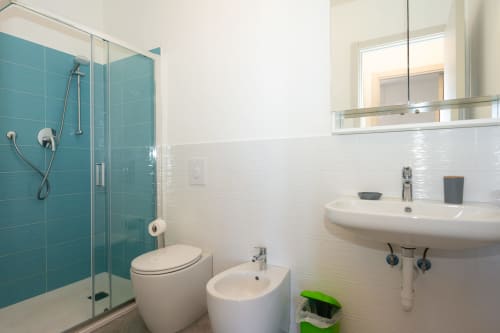 Bagno moderno con doccia in piastrelle turchesi, lavabo bianco, bidet e toilette dell'appartamento Welcome Holiday a Varigotti, Finale
