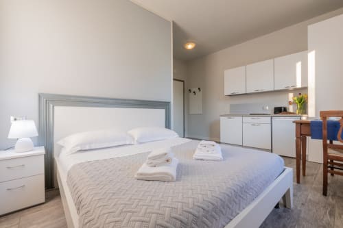 Moderna camera studio a Prince Garda Solarolo con letto, angolo cottura, zona pranzo e arredi bianchi