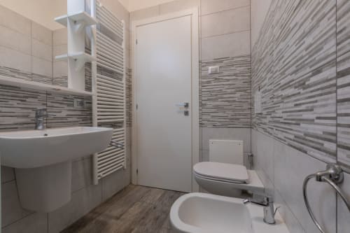 Moderno bagno dell'hotel Prince Garda a Solarolo con piastrelle a righe, lavabo bianco, WC e scaldasalviette