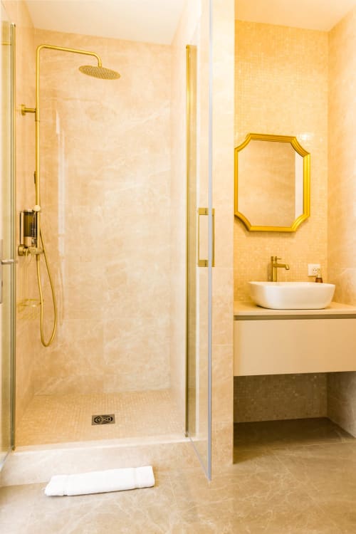 Bagno lussuoso con rubinetteria dorata, doccia in marmo, lavabo bianco a bacinella e specchio decorativo all'Hôtel Villa Martini