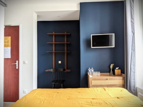 Chambre d'hôtel moderne aux Maisons Delphine avec lit jaune, mur d'accent bleu marine, bureau en bois et TV murale
