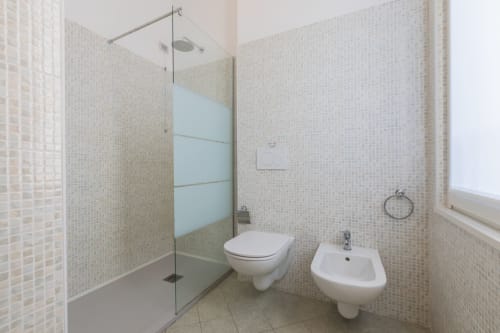 Bagno moderno all'hotel Prince Garda di Solarolo con cabina doccia in vetro, WC, bidet e pareti rivestite in mosaico color crema.