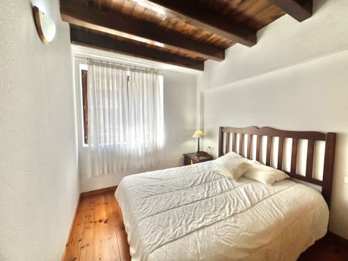 Dormitorio acogedor con vigas de madera, ropa blanca y piso de madera en el apartamento Era Clau, Vielha