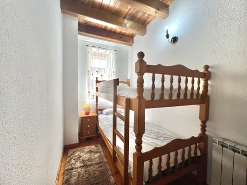 Dormitorio acogedor con litera de madera, vigas vistas y ventana en el apartamento Era Clau en Vielha, Pirineos