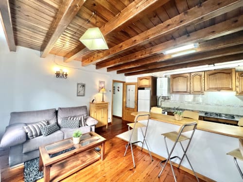 Apartamento moderno en Vielha con vigas de madera, sofá gris, cocina, comedor y vistas a la montaña. ERA CLAU HOMES
