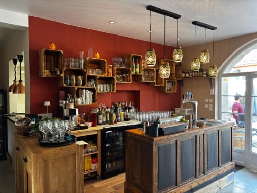 Clos De La Gourmandiere bar with red accent wall, wooden shelving, pendant lights, and counter seating in Saint-Lothain