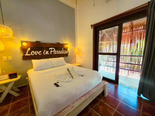 Habitación moderna del Hotel 40 Cañones en Mahahual con cama queen, letrero de neón 'Love in Paradise', cabecero de madera y cristal