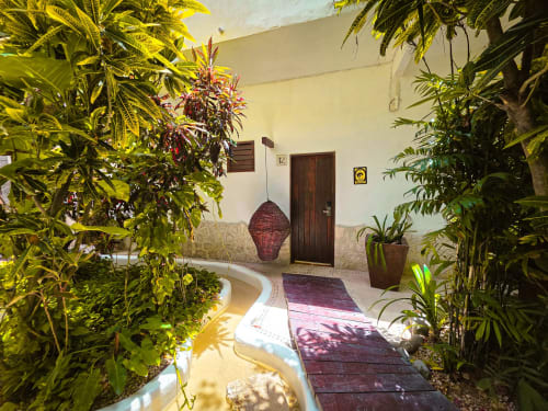 Entrada tropical del Hotel 40 Cañones en Mahahual con plantas exuberantes, puerta de madera y camino de azulejos
