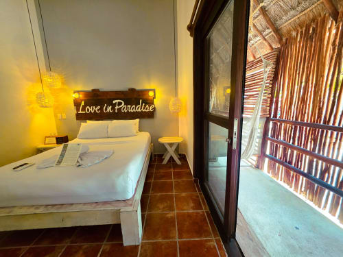 Habitación luminosa en Hotel 40 Cañones, Mahahual, con letrero 'Love in Paradise', cama blanca, iluminación cálida y acceso a balcón