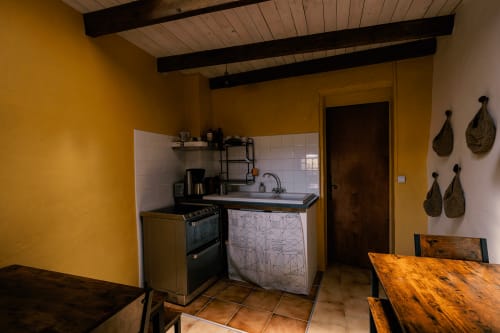 Cuisine jaune vif du Domaine de Cabrières avec cuisinière, évier, table à manger et plafond aux poutres rustiques à Saint-Jean-du-Gard.