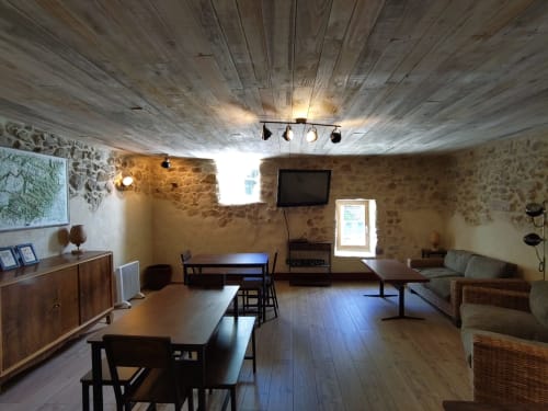 Salle commune rustique en pierre du Domaine de Cabrières avec poutres apparentes, salle à manger et coin détente