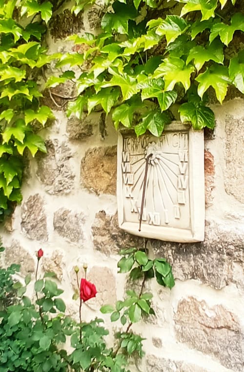 Mur de pierre rustique aux Gîtes Du Couvent avec lierre grimpant, cadran solaire et roses rouges en Ardèche
