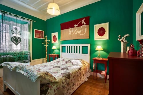 Quarto vibrante em verde na vila SOTAM Country House, com cama branca, detalhes em bordô, assoalho em madeira e arte decorativa